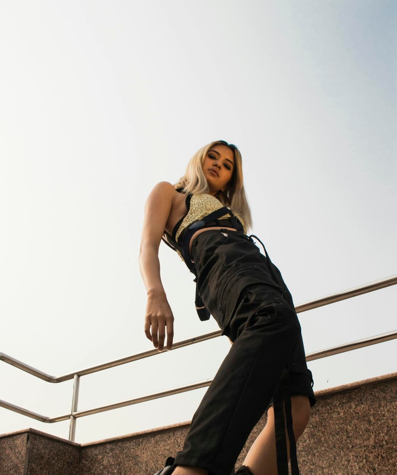 A stylish fashion model poses with a low angle shot, showcasing trendy attire in an outdoor urban setting.