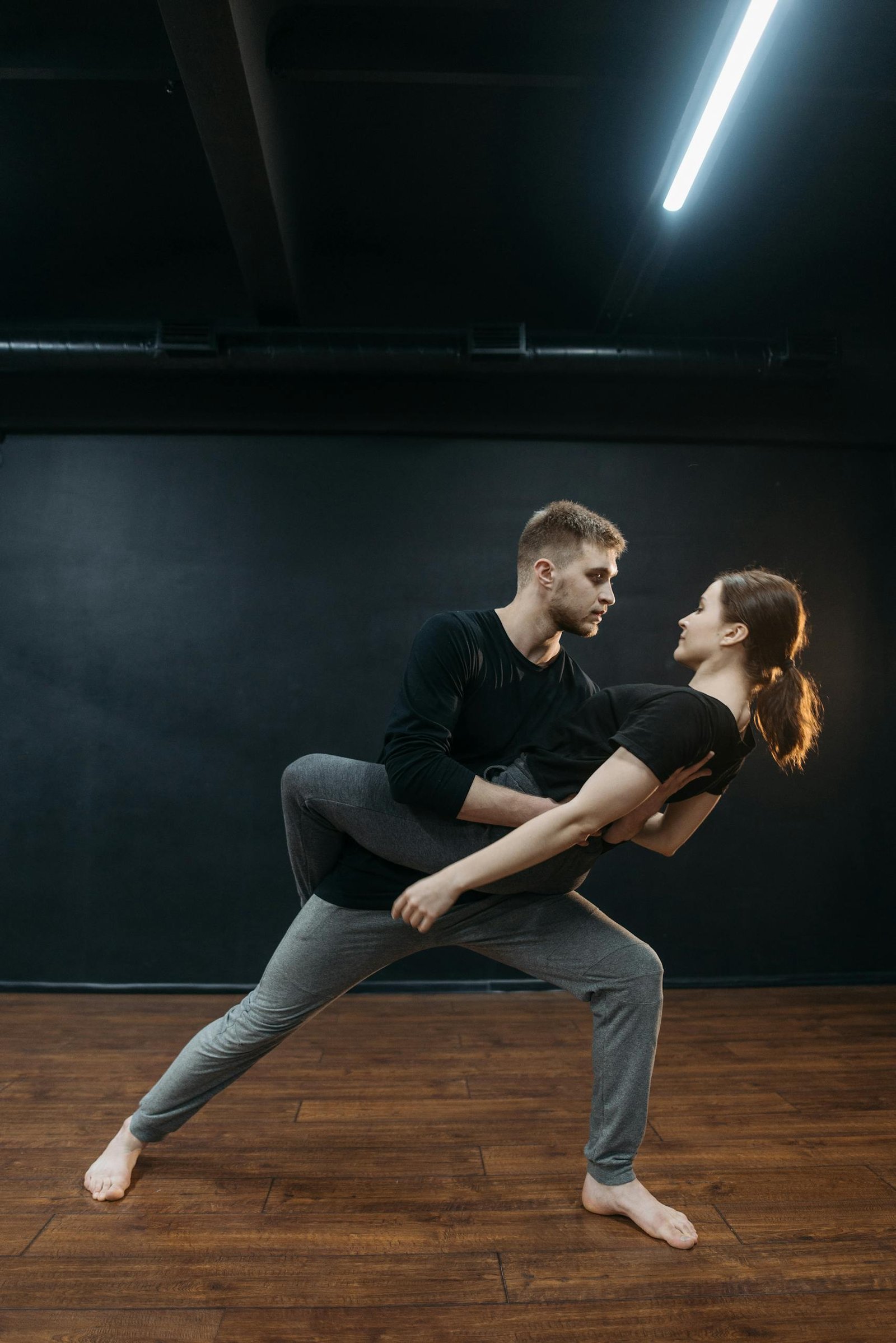 A couple performing a graceful dance pose in a studio with wooden floors.